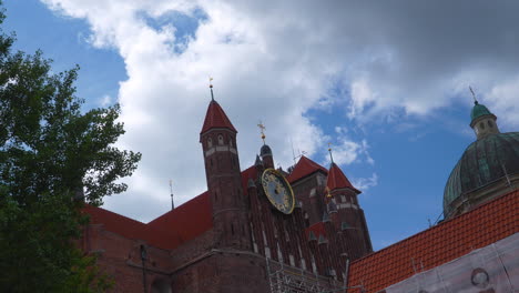 close-up of st. catherine’s church clock tower against partly cloudy sky in gdańsk