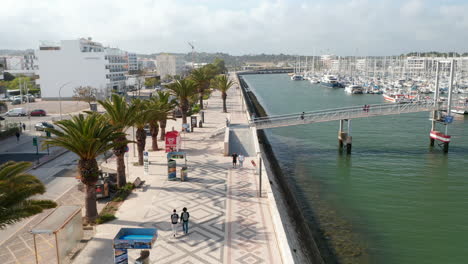 Aerial-view-of-Lagos-Algarve-streets,-drone-lowering-down-to-harbor-canal,-Portugal,-day