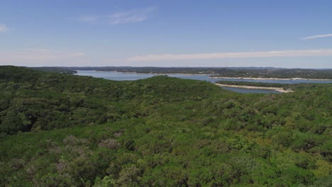 Drone-footage-flying-across-green-trees-with-a-beautiful-lake-view-in-the-distance