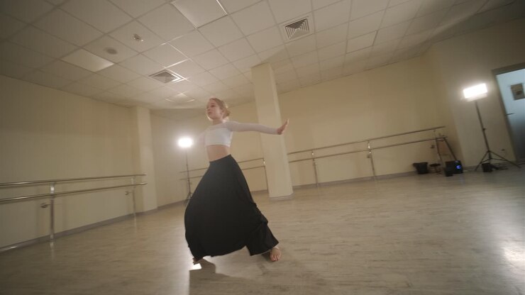 un grupo de jóvenes estudiantes de ballet con ropa de baile negra practicando posiciones en un amplio estudio de ballet con pisos de madera y barras montadas en la pared. expresiones enfocadas y movimientos sincronizados.