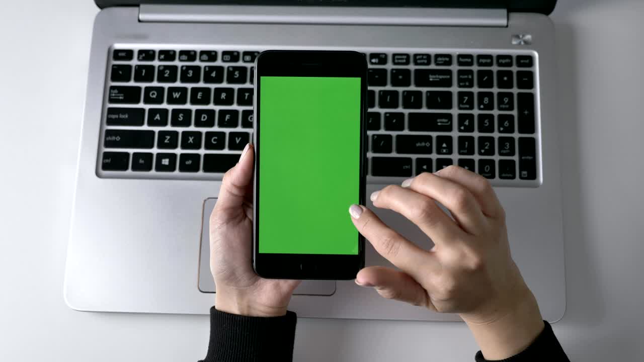 manos femeninas desplazándose en la pantalla táctil del teléfono inteligente. pantalla verde, concepto chromakey, portátil en el fondo. top shot 60 fps