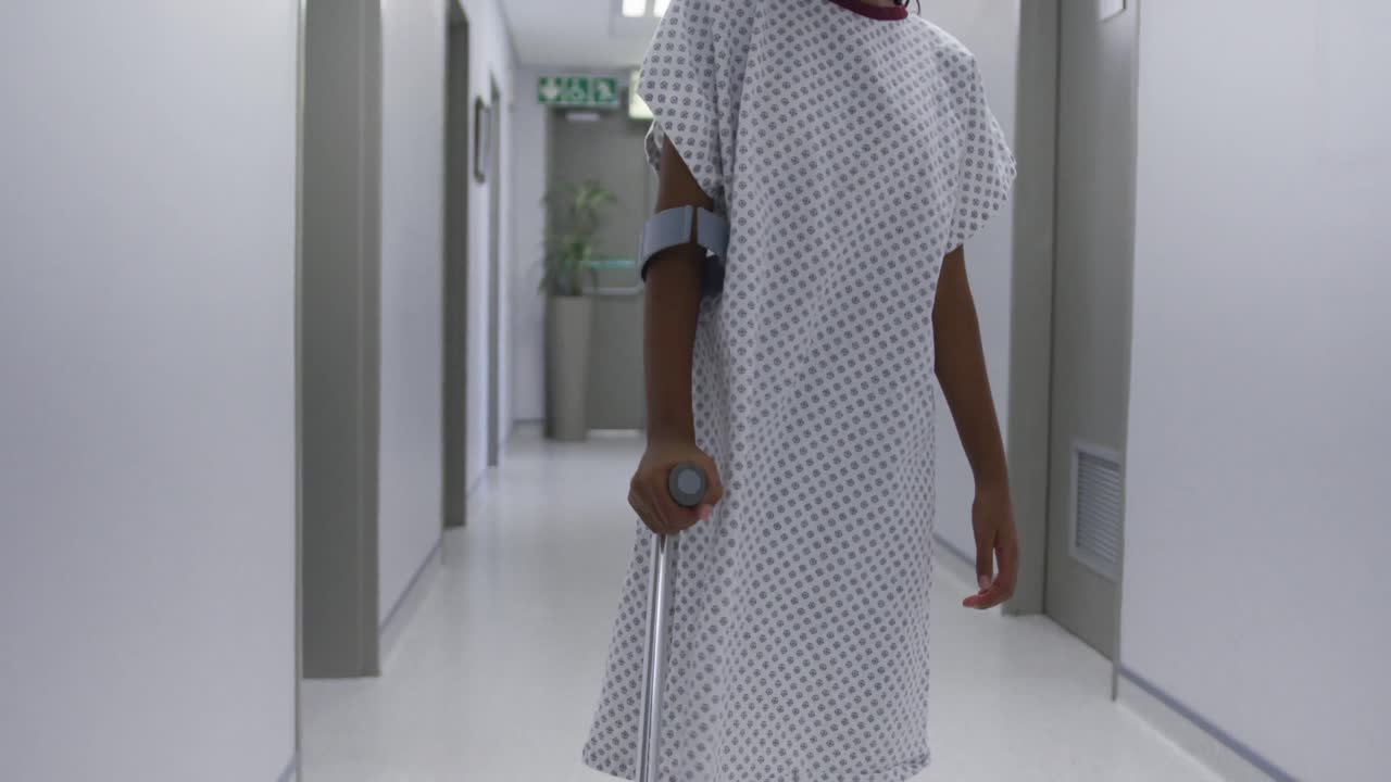 triste chica de raza mixta caminando con muletas por el corredor del hospital