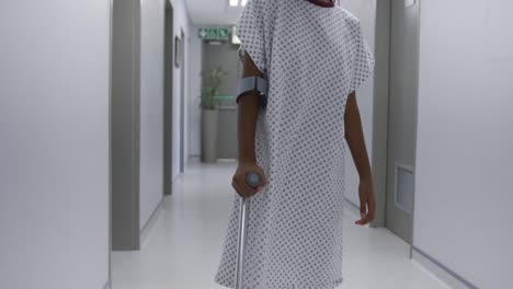 sad mixed race girl walking with crutches through hospital corridor