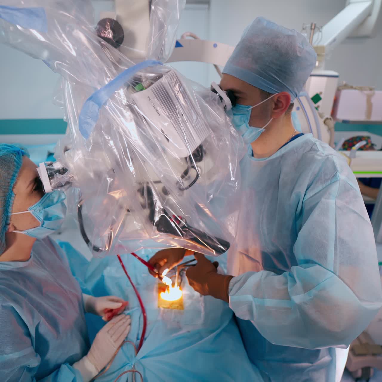 Neurosurgical department. Doctor works with sterile medical instruments on a patient in the operating room and observes into the microscope. Nurse assists surgeon.