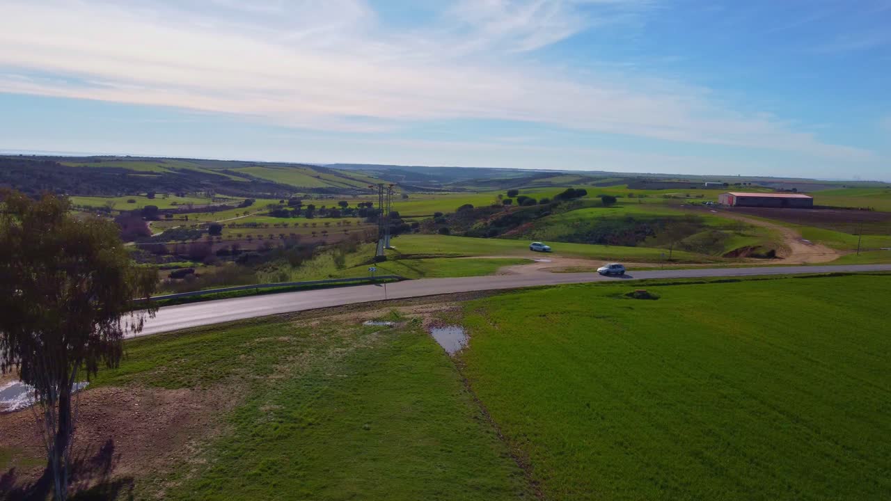 빈 도로를 운전하는 외로운 흰색 자동차는 푸른 초원과 농작물을 둘러싸고 있습니다.