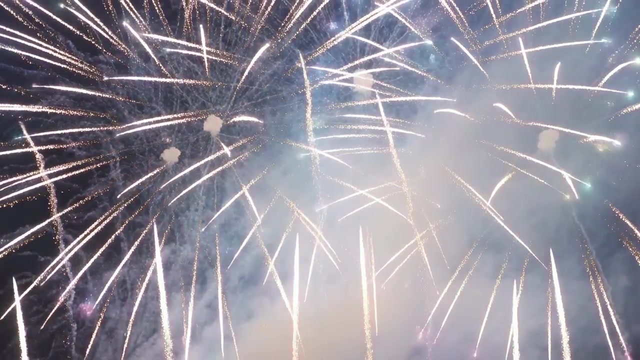 Le prime cariche detonano, i fuochi d'artificio si espandono in esplosioni a più livelli nel cielo notturno, creando fumo.