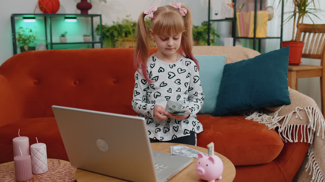niña pequeña contando dinero billetes de dólar para necesidades futuras en el escritorio de casa con computadora portátil, alcantarillado