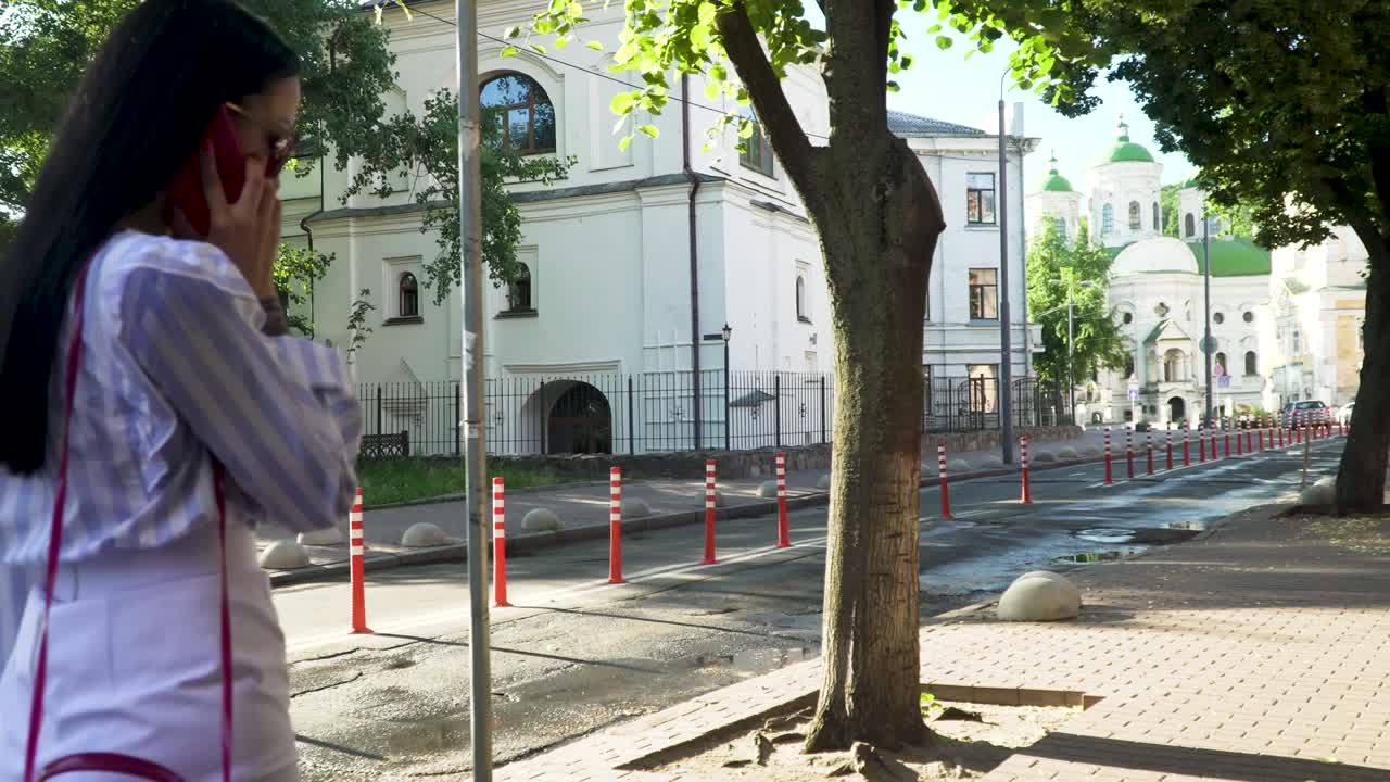 Elegant woman in white clothes talking on phone and walk at urban street