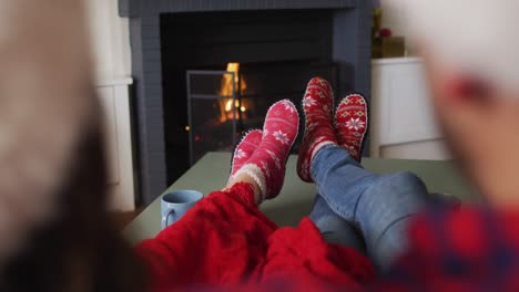 feet of caucasian couple sitting on sofa, wearing christmas socks and santa hats