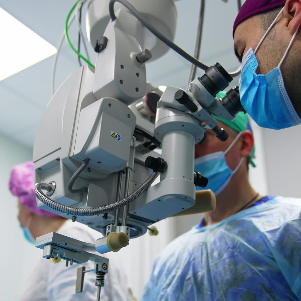 Complicado dispositivo tecnológico para cirugía ocular. Dos cirujanos mirando por los binoculares durante la operación. Vista en ángulo bajo