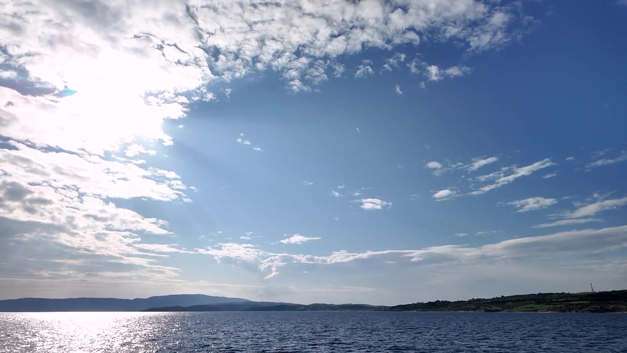 廣闊的海洋與天空景觀，雲朵點綴其中。陽光在水面上閃耀，晴朗天氣下遠處的陸地清晰可見。