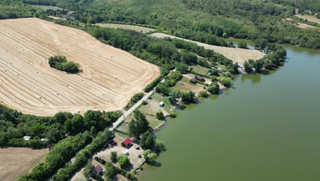 Cozy-camping-cottage-land-between-water-and-hay-farm-with-scattered-bales,-drone