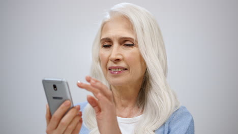 Senior-woman-scrolling-online-indoors.-Mature-lady-watching-news-in-cellphone.
