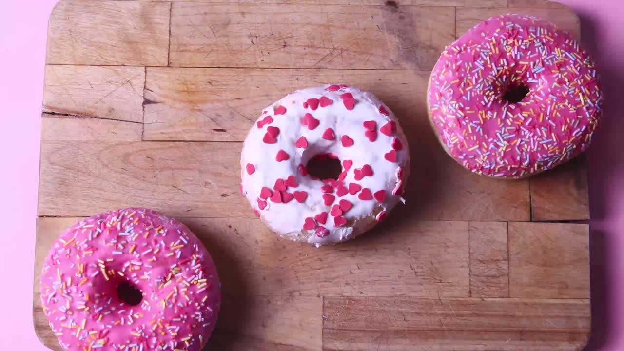 Tasty rotating pink donuts, stop motion on pink background. Pink glazed donut with sprinkles, time-lapse on pink background.