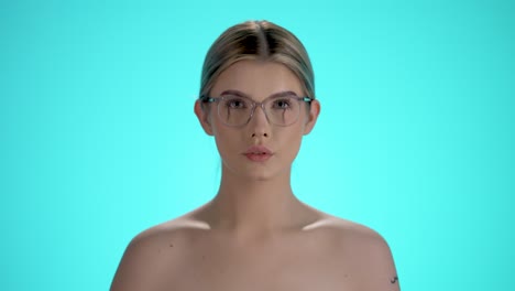 Static-medium-shot-of-a-young-pretty-woman-putting-on-her-glasses-for-a-clear-view-and-looking-at-the-camera-in-front-of-turquoise-background-in-slow-motion