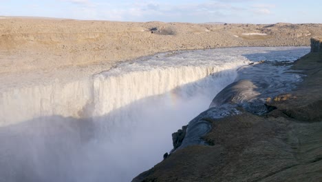 Majestic-Dettifoss-waterfall-in-Iceland-with-powerful-water-flow-and-mist,-featuring-a-small-rainbow