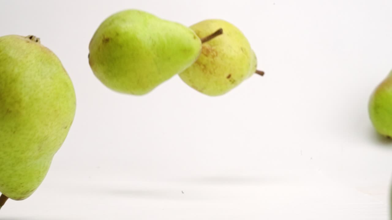 Whole pears bouncing and rolling onto white studio backdrop in 4k slow motion