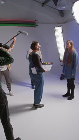 Vertical-Video-Of-Female-Assistant-Using-Clapperboard-As-Actors-Shoot-Movie-Or-Video-In-Studio-With-Film-Crew-And-Director-Shot-In-Real-Time-2