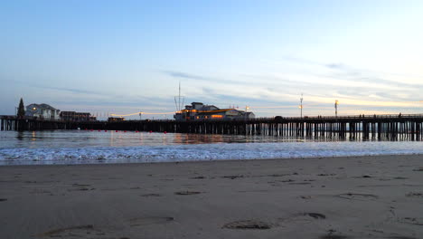 a scenic california sand beach with stearns wharf pier beyond the ocean waves illuminated by lanterns and lights at sunset in santa barbara