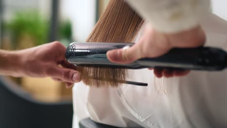 handheld view of hairstylist using straightener at work