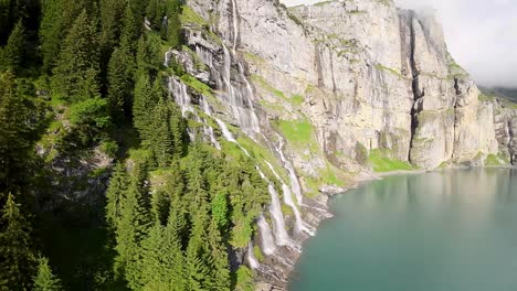 aerial flight next to a beautiful big waterfall on a mountain landscape, drone flying over a blue lake - oeschinen lake, switzerland