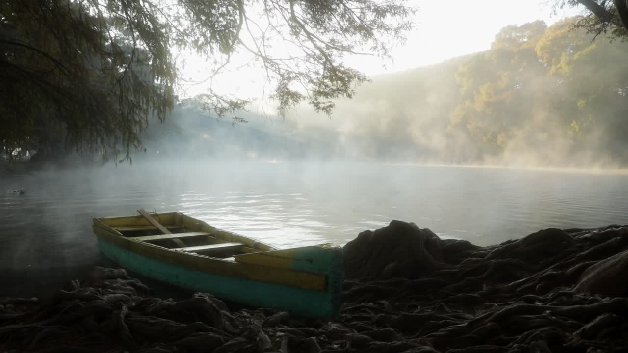 A boat floats in the beautiful sunrise of a lake surrounded by the rays of the sun and the mist.Un bote flota en el hermoso amancer del lago de Camécuaro, rodeado por los rayos del sol y la neblina.