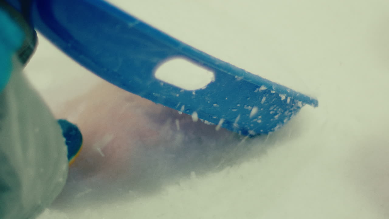 niño jugando al aire libre durante una tormenta de nieve usando botas de lluvia azules y usando una caja de plástico