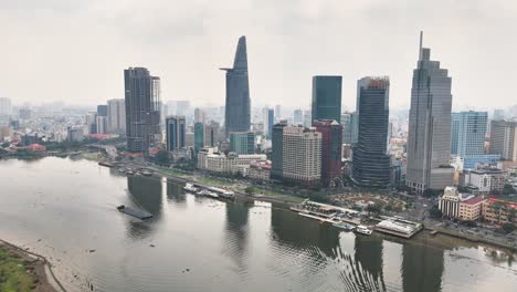 drone view over central ho chi minh city, vietnam, featuring the saigon river and iconic skyline with bitexco financial tower and landmark 81 reflecting in the water under bright daylight