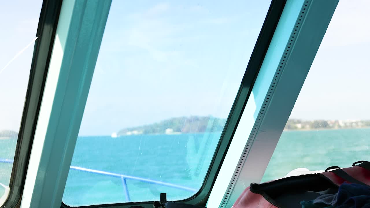 푸켓의 푸르키즈색 물을 가로질러 평온한 보트 여행, 창문에서 찍은 조용한 바다 풍경과 먼 섬을 보여주는