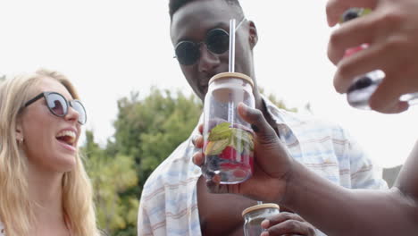 joven mujer caucásica y hombre afroamericano brindis con bebidas refrescantes al aire libre