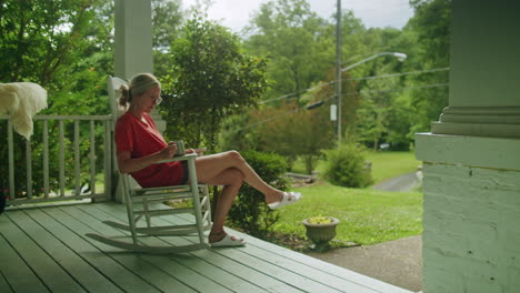 young woman sitting on a rocking chair on her front porch, relaxing and drinking tea