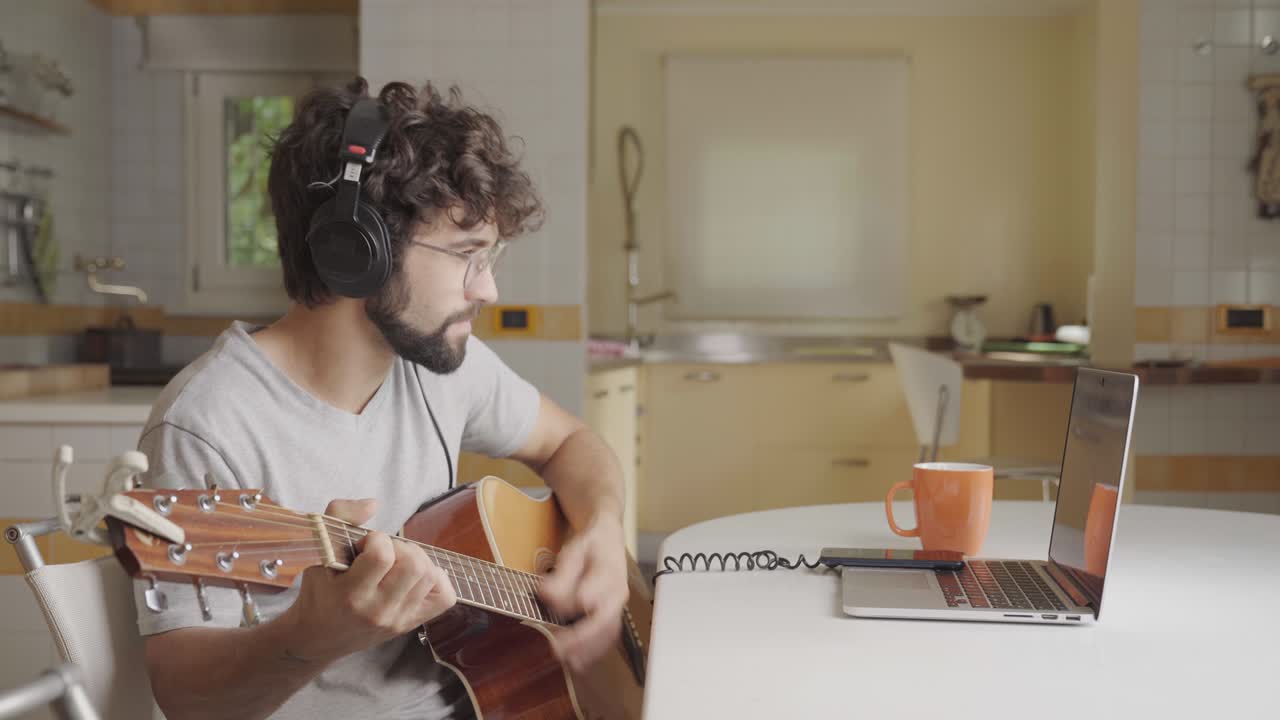 young adult man learning guitar in online class with distant teacher education