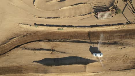 ascending over a motocross racetrack as a water tank prepares the track for the race - straight down aerial view