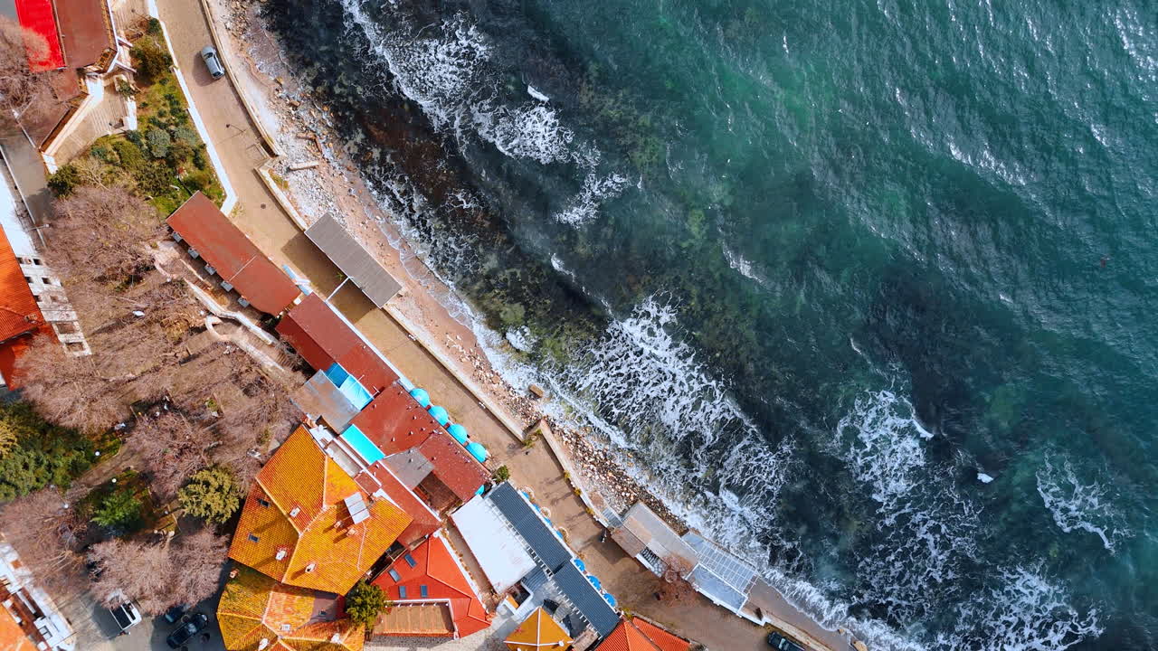 Vista aerea dall'alto di onde marine e tetti. Inquadratura zenitale di onde turchesi che si infrangono sul litorale cittadino.