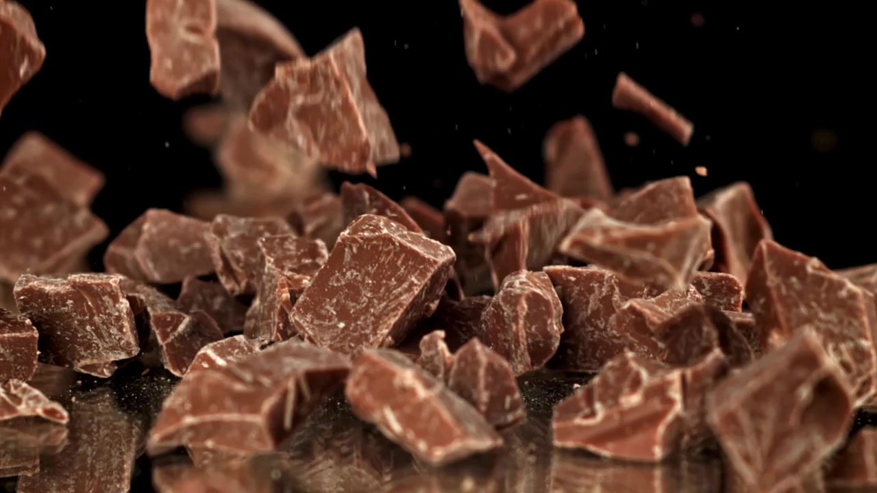 Pezzi di cioccolato in caduta al rallentatore su una superficie riflettente nera