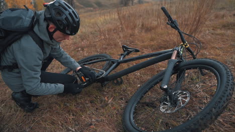 atleet man die het pedaal van een mountainbike op het platteland repareert