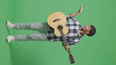 full body of asian teenager with guitar smiling and pointing to the side on green screen background