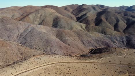 Aerial:-A-lonely-dirt-road-twists-through-endless-rustic-hills,-Chile