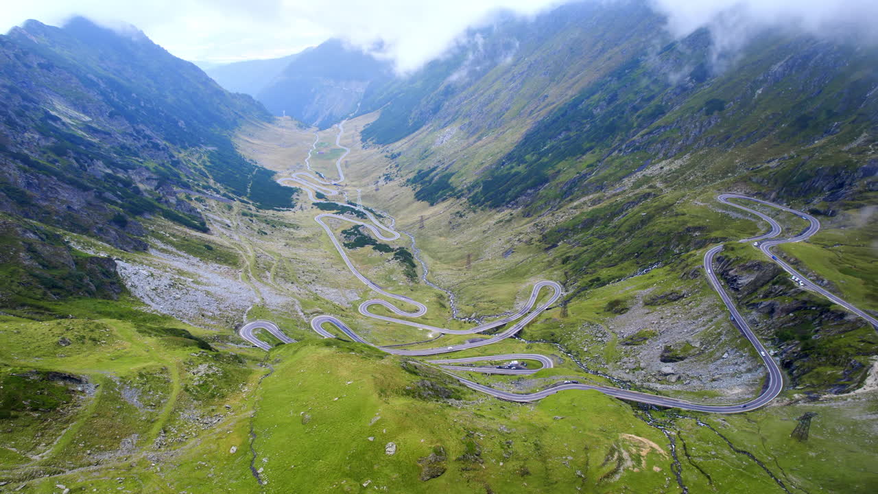 Vista aerea con drone della natura in Romania. Strada Transfăgărășan sui Monti Carpazi con auto in movimento visibili tra le nuvole, pendii rocciosi con vegetazione