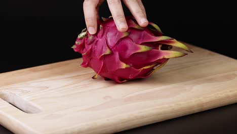 hands manipulate dragon fruit on wooden board