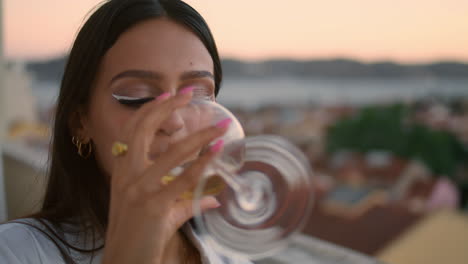 una mujer hermosa haciendo sonar un vaso en un primer plano en la terraza al atardecer. una mujer bebiendo vino.
