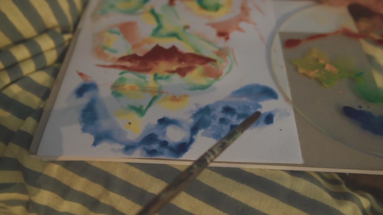 예술적인 여성은 긍지와 만족감으로 그녀의 마음 가까이에 그녀의 활기차고 다채로운 그림을 완성합니다.