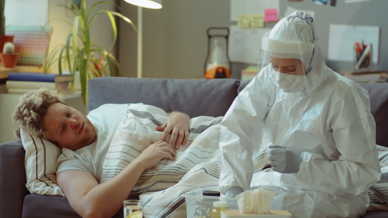 врач в защитном костюме объясняет план лечения больному человеку дома