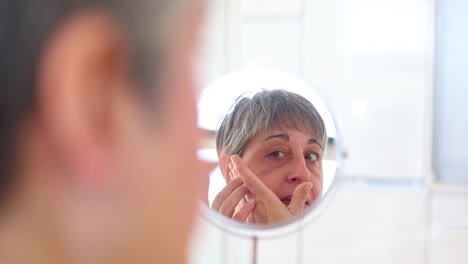 mujer mayor en bata de baño aplicando crema facial