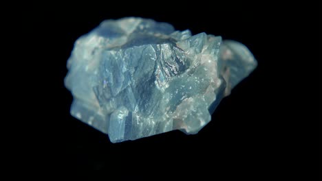girando sin problemas un mineral azul cielo (calcita azul) frente al fondo negro