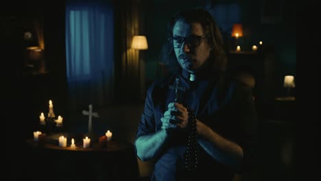 video capturing a priest standing in the dark room with beads and a cross in his hands praying with