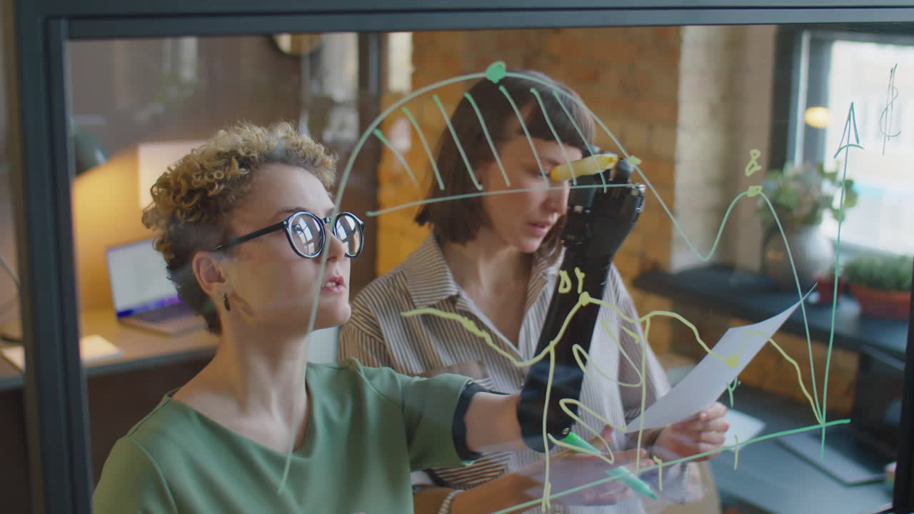 Diverse Businesswomen Drawing Graph on Glass Wall during Office Workday