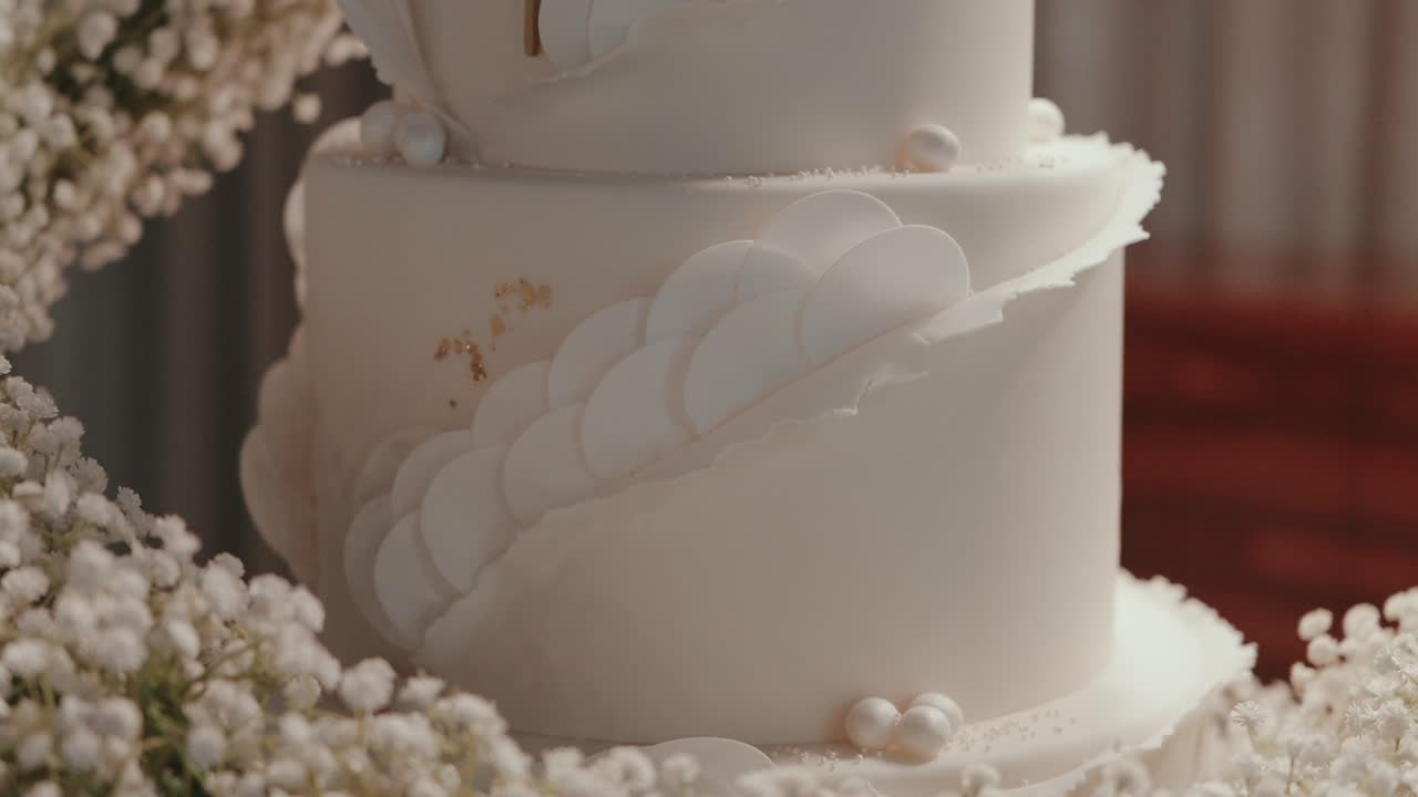 Close up of elegant white wedding cake with pearl details and floral sugar patterns