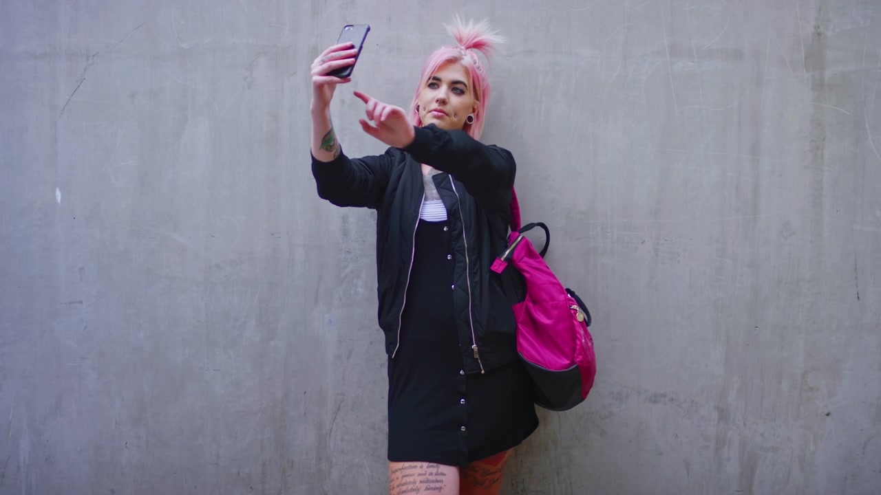 Giovane donna con i capelli rosa che si scatta un selfie contro un muro di cemento
