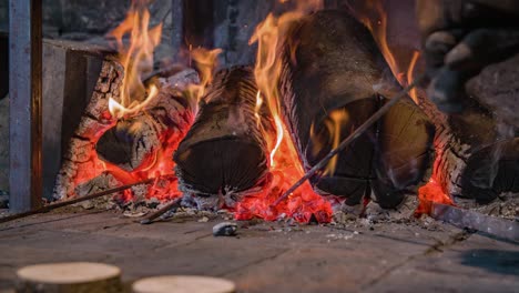 primer plano de una persona con guantes cerca de un horno de leña calentando un palo de hierro con cenizas ardientes